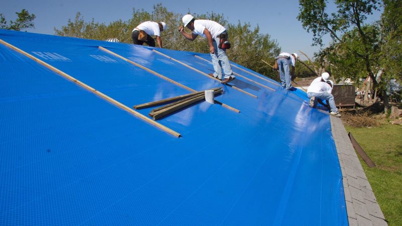 Crew fastening a blue tarp over a storm-damaged roof in Texas