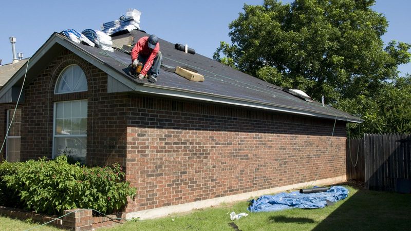Roofer installing new shingles on a brick home