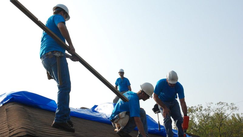 Crew spreading a blue emergency tarp across a roof after Hurricane Ike in Texas
