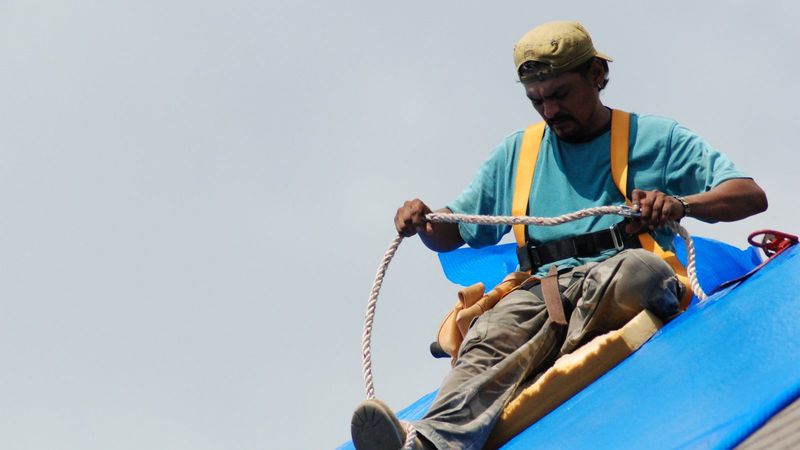 Worker in a safety harness securing a blue tarp after Hurricane Ike in Texas