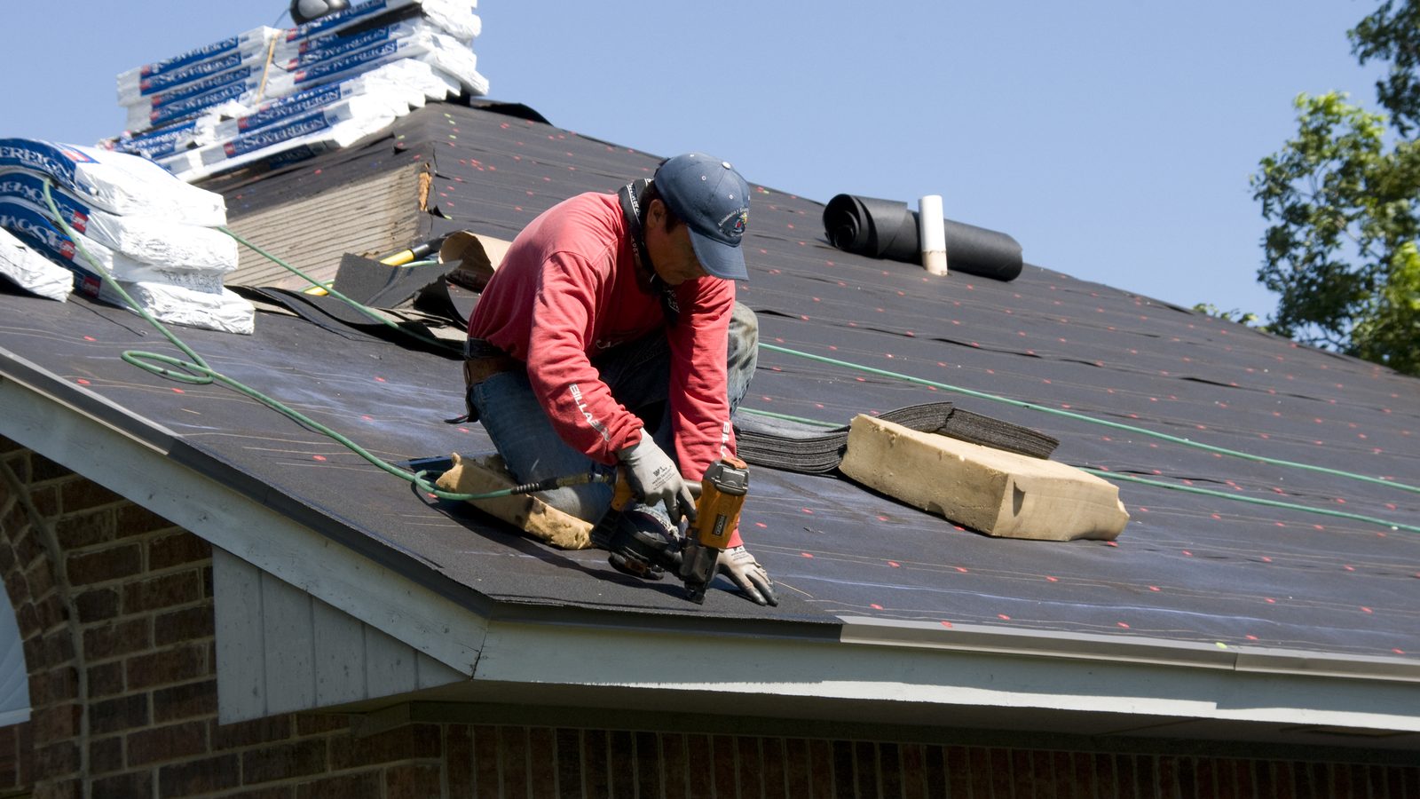 Roofer installing new shingles on a brick home