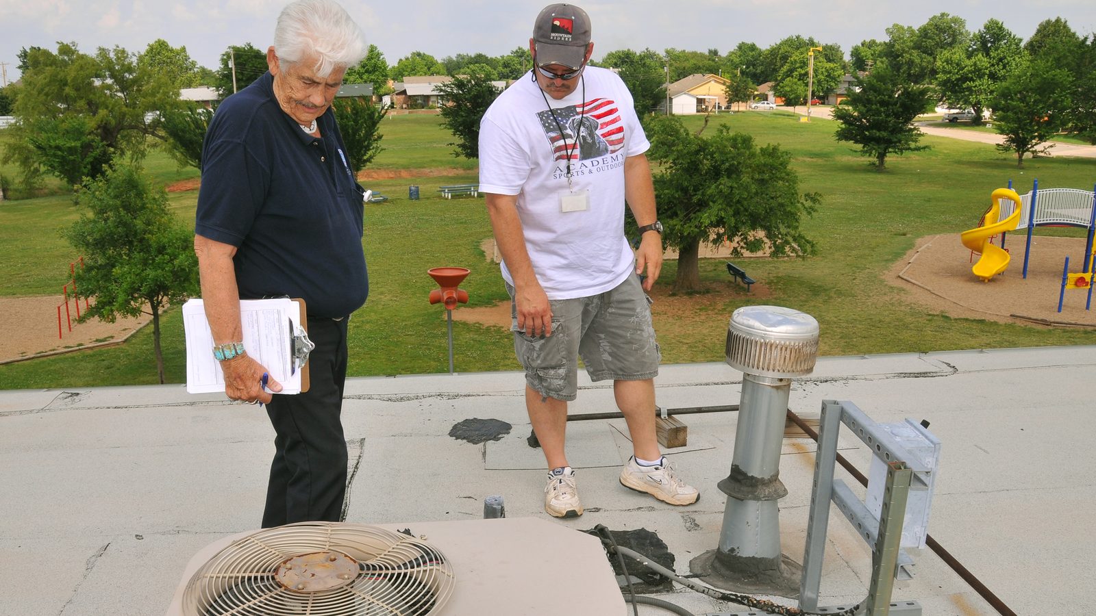 Inspectors checking a rooftop AC unit and vents for hail damage