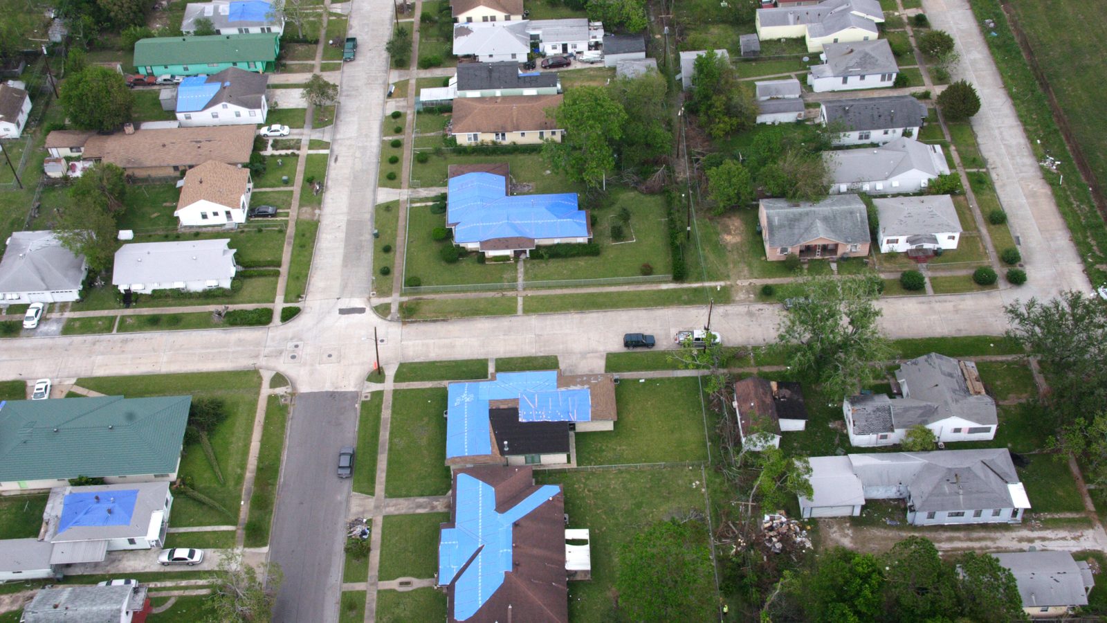 Aerial view of a Texas neighborhood with blue tarps on wind-damaged roofs