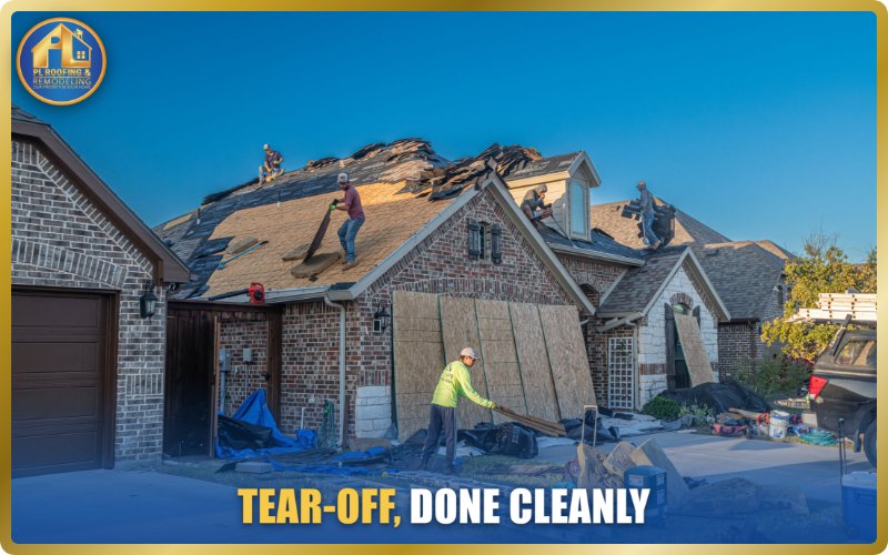 Roofing crew stripping the old shingles from a Texas brick home: torn-off shingles stacked on the roof, bare decking exposed, plywood shielding the siding and tarps covering the landscaping and driveway