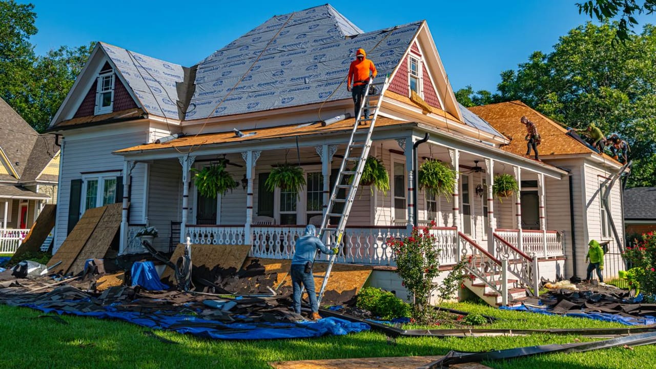 Storm Bolt Roofing crew completing an asphalt shingle roof replacement on a Houston-area home, with synthetic underlayment installed and the yard protected by tarps